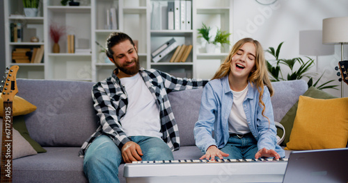 Lovely daughter play piano with father in the living room with happy moment. Child learning playing piano from her father. Weekend activity happy family lifestyle concept