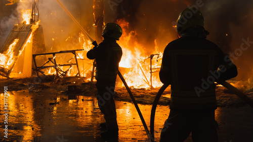 Two firefighters in action, fighting very strong fire, against light, dangerous, extinguishing fire