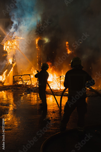Two firefighters in action, fighting very strong fire, against light, dangerous, extinguishing fire