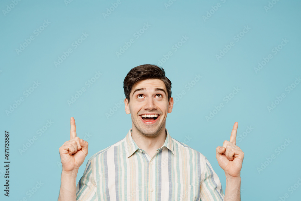 Young happy smiling man wear striped shirt casual clothes point index finger overhead on area mock up copy space isolated on plain pastel light blue cyan background studio portrait. Lifestyle concept. Young happy smiling man wear striped shirt casual clothes point index finger overhead on area mock up copy space isolated on plain pastel light blue cyan background studio portrait. Lifestyle concept.