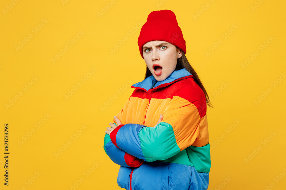Side view young frowning woman she wears padded windbreaker jacket red hat casual clothes hold hands crossed folded look camera isolated on plain yellow background studio portrait. Lifestyle concept. Side view young frowning woman she wears padded windbreaker jacket red hat casual clothes hold hands crossed folded look camera isolated on plain yellow background studio portrait. Lifestyle concept.
