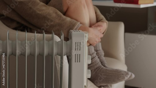 Young woman in warm clothes sit alone shivering from cold on chair in unheated apartment without central heating due debt. Unhealthy female feeling discomfort try to warming up indoor.