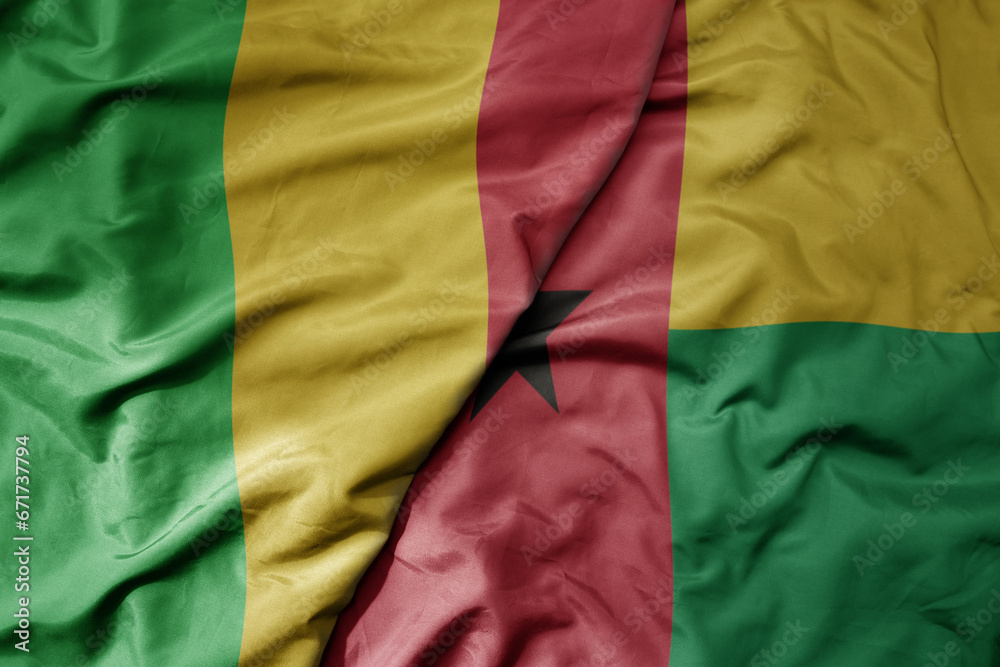 big waving national colorful flag of mali and national flag of guinea bissau .
