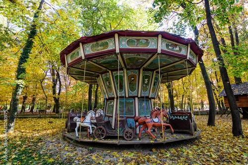 Old wooden painted children carousel surrounded by old large yellow and green trees in the Village Museum in Herastrau Park in Bucharest, Romania in a sunny autumn day.