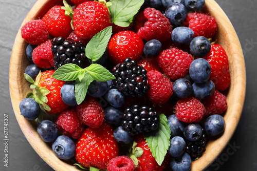 Many different fresh ripe berries in wooden bowl on black table  top view