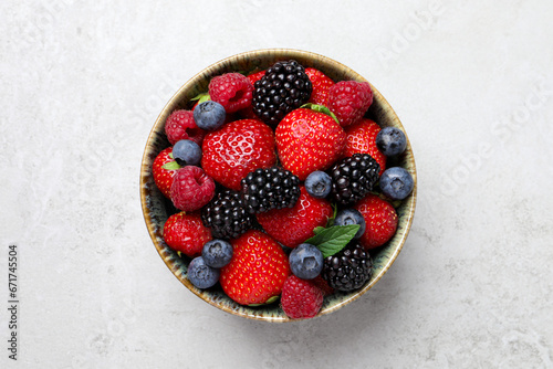 Different fresh ripe berries in bowl on light grey table, top view photo