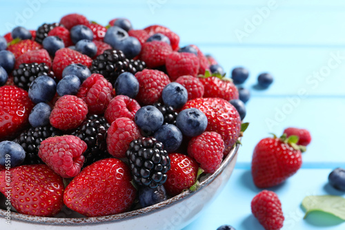 Different fresh ripe berries in bowl on light blue wooden table, closeup
