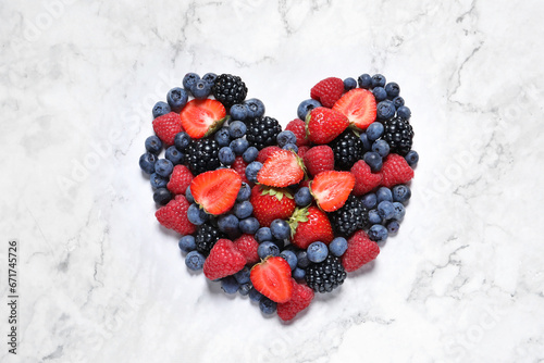 Heart made of different fresh ripe berries on white marble table, top view photo