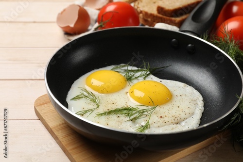 Frying pan with tasty cooked eggs, dill and other products on light wooden table, closeup
