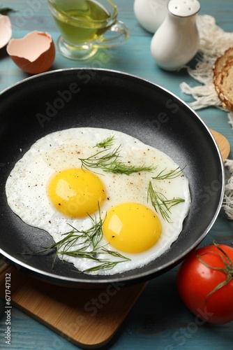 Frying pan with tasty cooked eggs, dill and other products on light blue wooden table, closeup