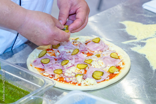 The process of making pizza stuffed with ham, cheese and pickles. The chef's hands lay out the ingredients on the pizza. Pizzeria work