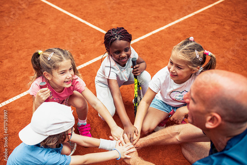 Children and their coach come together in a huddle on the tennis court photo