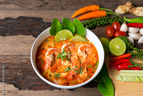 Tom Yum Goong or Shrimp soup spicy sour Soup Traditional food in Thailand contains chili, lime,lemongrass, lime leaf, along with cooked rice in a white dish on the old wood background. photo
