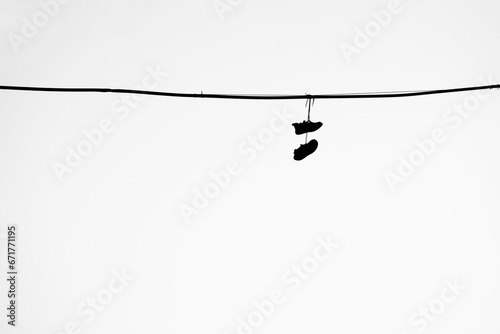 black silhouette of sneakers, Shoes hanging from a telephone wire on white sky background. Old sneakers hang on an electric wire on a summer day.  isolated on white background. illustration. photo