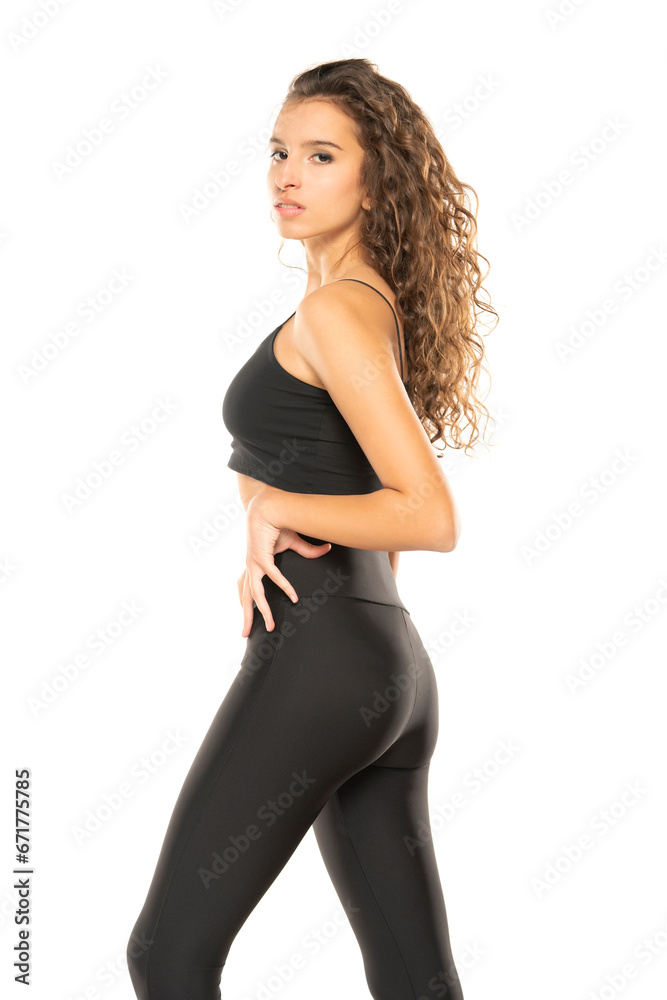 Young curly brunette posing in black leggings and shirt on a white background Young curly brunette posing in black leggings and shirt on a white background