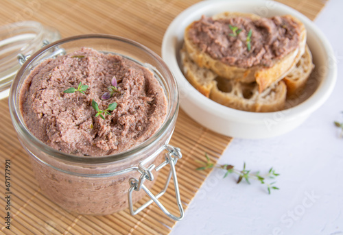 Vegan spread made with lentils and nuts on a rustic bread slice and in a glass jar, decorated with rosemary. Vegan dipping.
