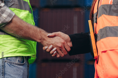 People at work: man and woman hand shaking at shipping terminal with containers in background © vladdeep