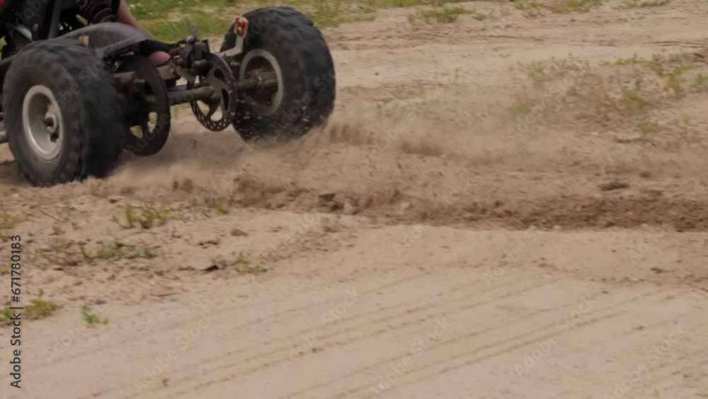 Close-up. The wheels of an ATV drive along a dirt road and throw sand out from under the wheels. Quad bike. The child turns sharply on the ATV, throwing sand in all directions. Close-up. The wheels of an ATV drive along a dirt road and throw sand out from under the wheels. Quad bike. The child turns sharply on the ATV, throwing sand in all directions.