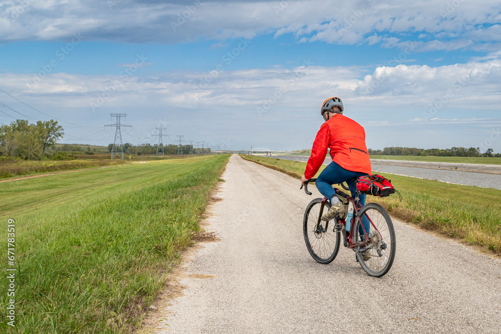 male cyclist is riding a gravel touring bike - biking on a levee trail along Chain of Rocks Canal near Granite City in Illinois male cyclist is riding a gravel touring bike - biking on a levee trail along Chain of Rocks Canal near Granite City in Illinois