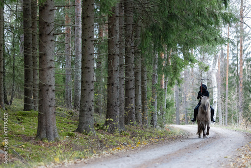 Reaper riding on gravel road in Autumn scenery. Ghost rider. Icelalandic horse. Halloween