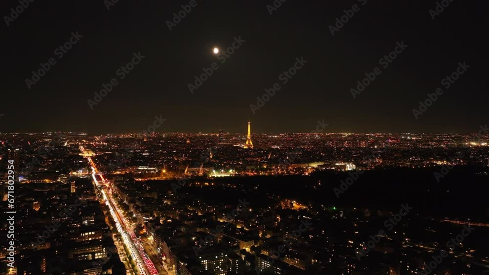 Aerial panoramic view of large city. Illuminated popular Eiffel Tower with rotating spotlight on top. Paris, France