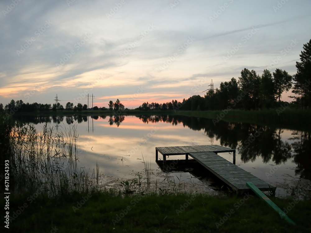 Sunset or sunrise on the lake in summer. Wooden bridge for fishing.