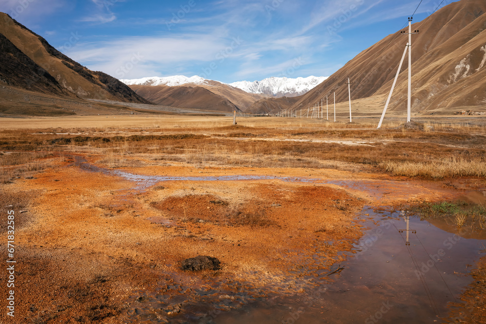 Rust-colored wetlands in the foreground of a vast mountainous expanse. Power lines trace a path across the untouched terrain