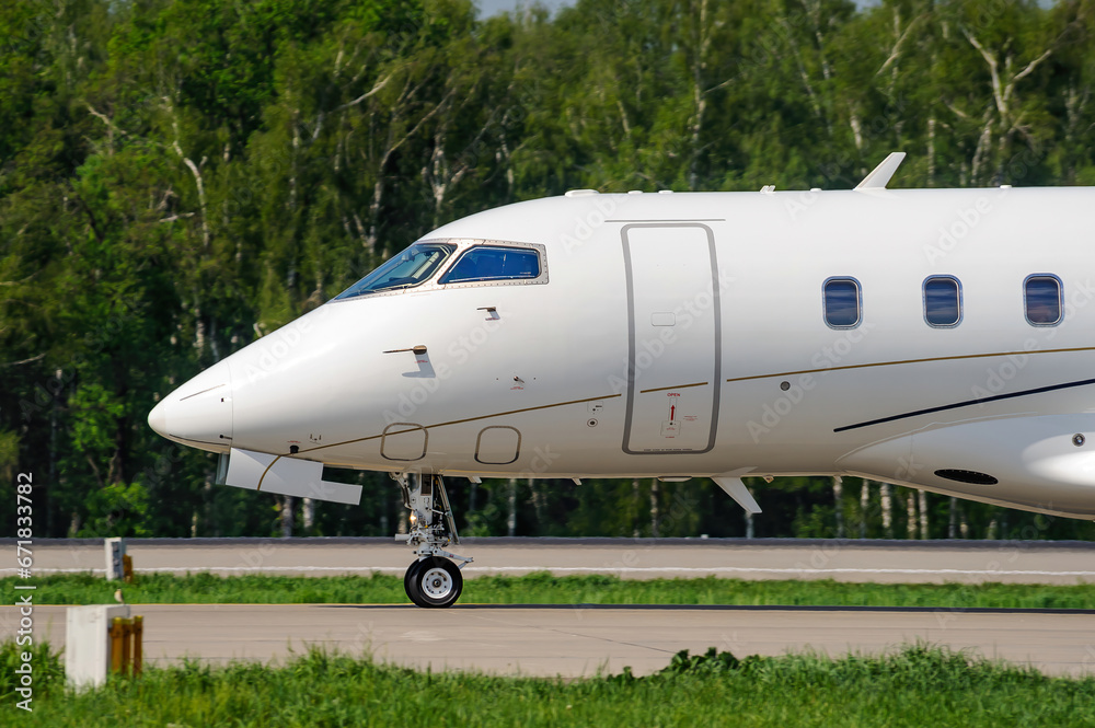 Close-up of the nose of a white passenger private business jet on the taxiway at the airport. The business jet is preparing to take off