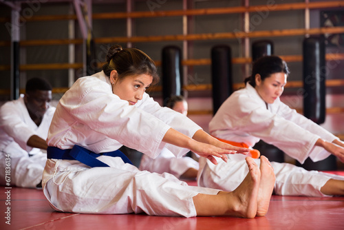 Multiracial group of people in kimono stretching on floor during karate training.
