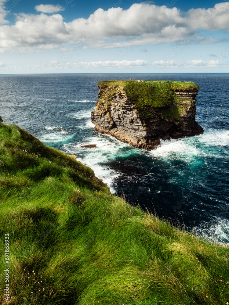 View on rough small island in the ocean from a cliff, Ireland, Kilkee area. Warm sunny day, blue cloudy sky. Travel, tourism and sightseeing concept. Irish landscape and coastline.