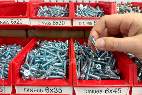 A hand takes a screw from a box close-up. Selection of screws of different sizes for strengthening or construction.