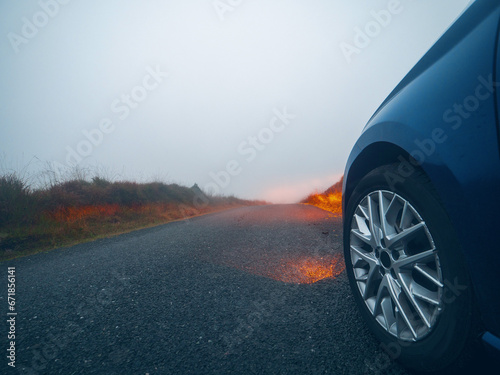 Car on a small narrow country road with high quality asphalt surface without marking at fog. Driving in dangerous conditions due to poor weather and low visibility in rural area. Selective focus.
