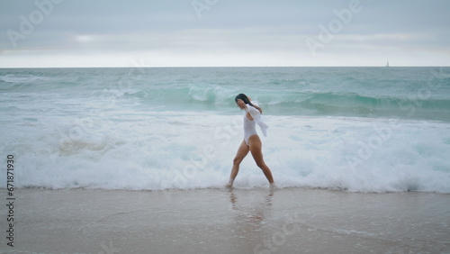 Woman walking ocean waves cloudy weekend. Girl stepping on sand beach sea water