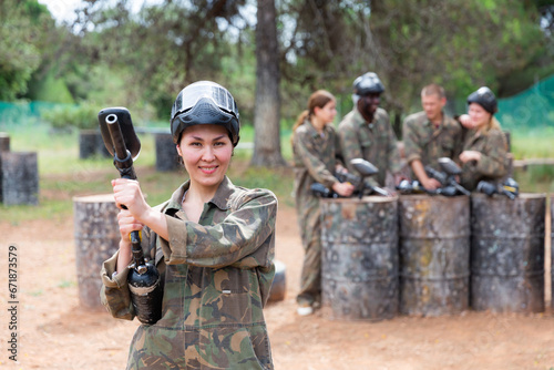 Happy woman wearing uniform and holding gun ready for playing with friends on paintball outdoor