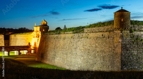Lighted main entrance of ancient Castle of San Pedro de Jaca, Italian-style pentagram-shaped fortress with turrets on corners of stone walls and bridge over moat in summer evening, Huesca, Spain