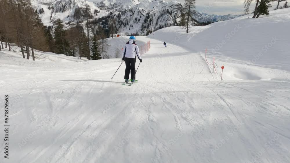 Following unknown lady skiing on a groomed ski track at picturesque alpine resort. Experienced female skier enjoys skiing during an active winter vacation among beautiful mountains of Austrian Alps. Following unknown lady skiing on a groomed ski track at picturesque alpine resort. Experienced female skier enjoys skiing during an active winter vacation among beautiful mountains of Austrian Alps.