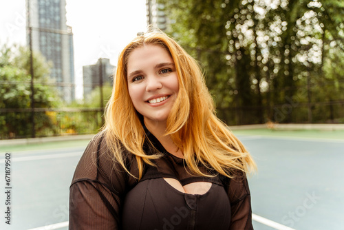 Smiling pretty woman in sports top posing on sports ground. Body positive, plus size, motivation