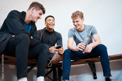 Fototapeta Naklejka Na Ścianę i Meble -  Sports, smartphone and friends relax in locker room after practice, exercise and training in gym. Wellness, fitness club and men on phone listening to music, audio and share track rest from workout
