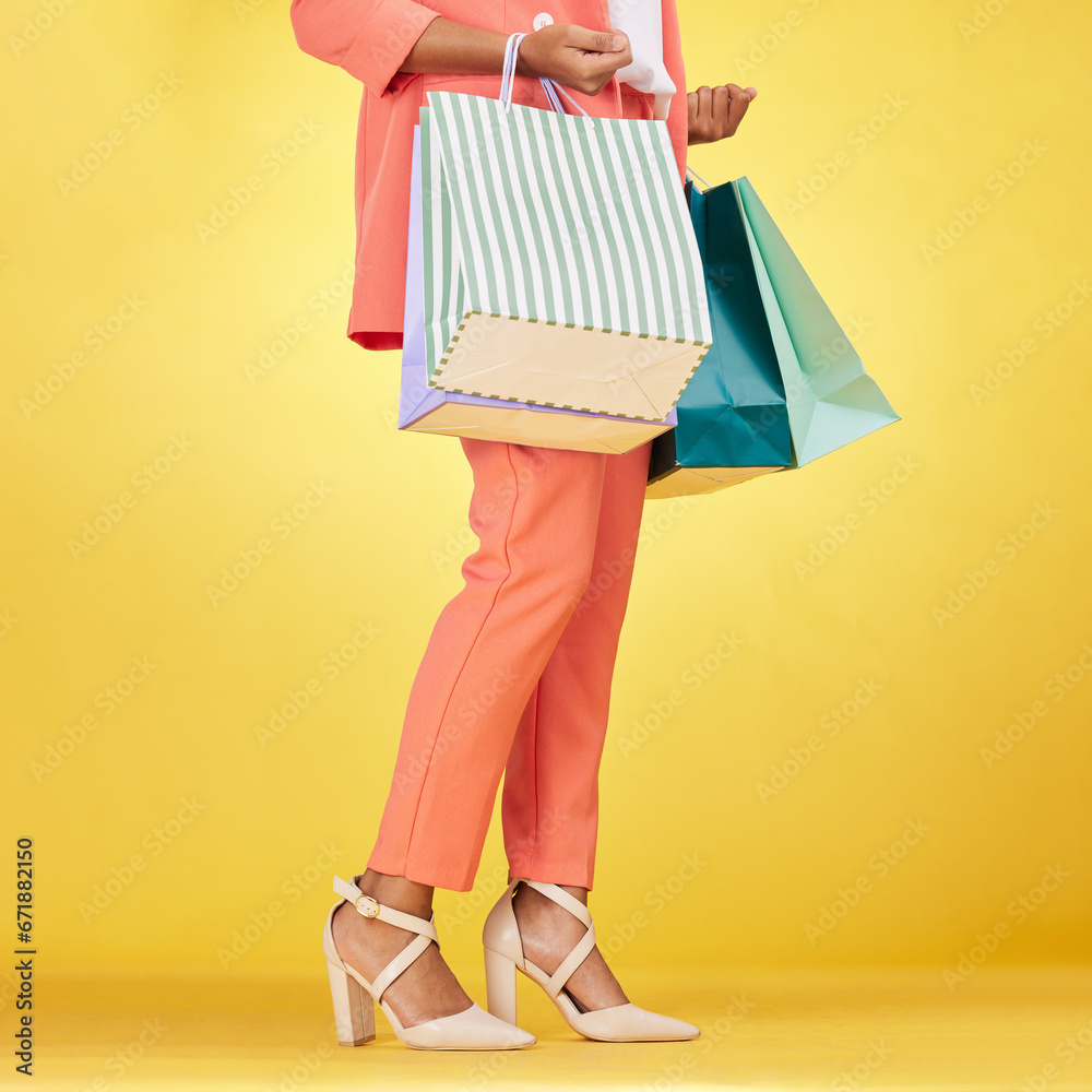 Legs, woman and shopping bag in studio for fashion, retail deal and financial freedom on yellow background. Closeup of customer, gift bags and discount from clothes store, shoes sales and promotion - obrazy, fototapety, plakaty 