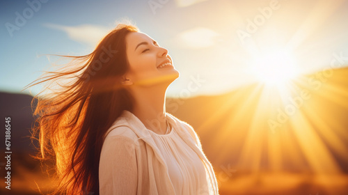 Young, red-haired woman smiles in a sunlit field, embracing nature's beauty and tranquility.