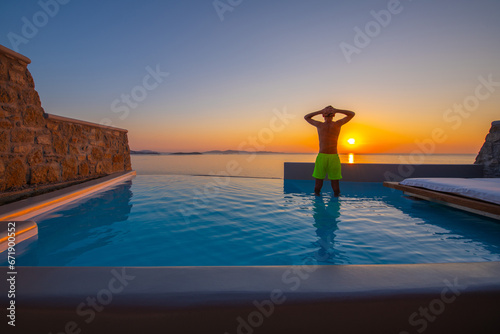 Tourist enjoys at the infinity swimming pool villa at sunset time, Mykonos, Greece © Kyrenian