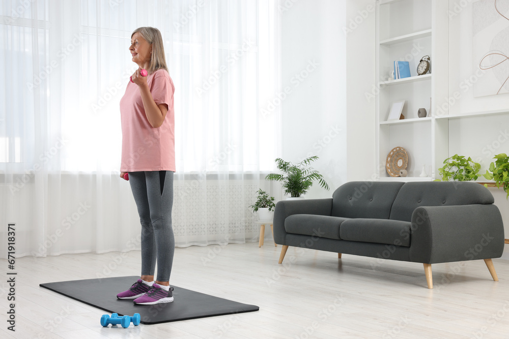 Senior woman exercising with dumbbells on mat at home. Sports equipment Senior woman exercising with dumbbells on mat at home. Sports equipment