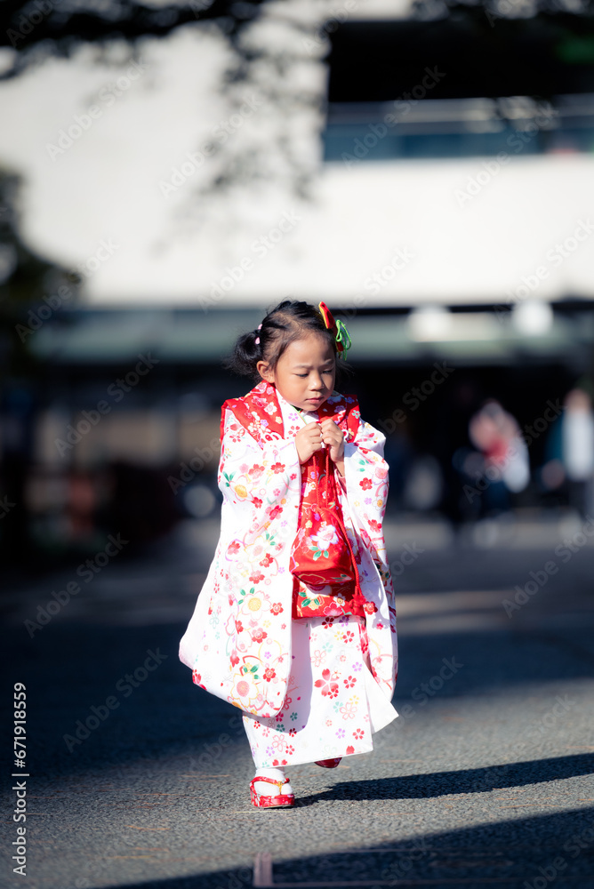 A toddler girl walking on the street wearing a red Japanese kimono. 
