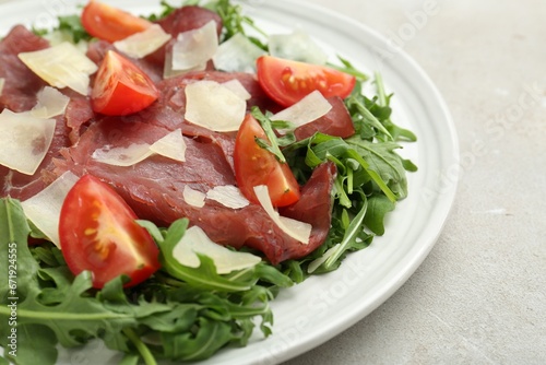 Delicious bresaola salad with parmesan cheese on light grey textured table, closeup