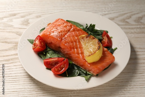 Tasty grilled salmon with tomatoes, lemon and basil on white wooden table, closeup