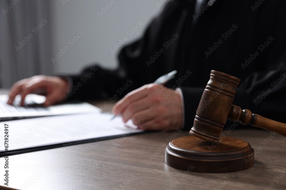 Judge with gavel writing in papers at wooden table, closeup - obrazy, fototapety, plakaty 