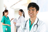 Portrait of a Young male Doctor with team in background.