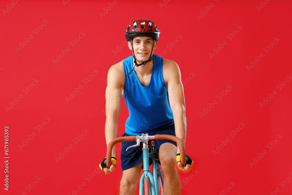 Young man riding bicycle on red background, front view - obrazy, fototapety, plakaty 