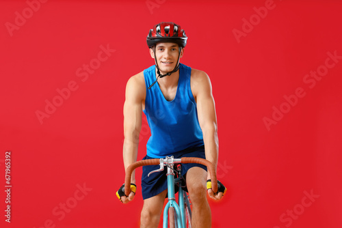 Young man riding bicycle on red background, front view © Pixel-Shot