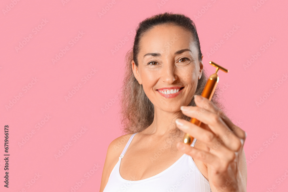 Beautiful mature woman using face massage roller on pink background Beautiful mature woman using face massage roller on pink background